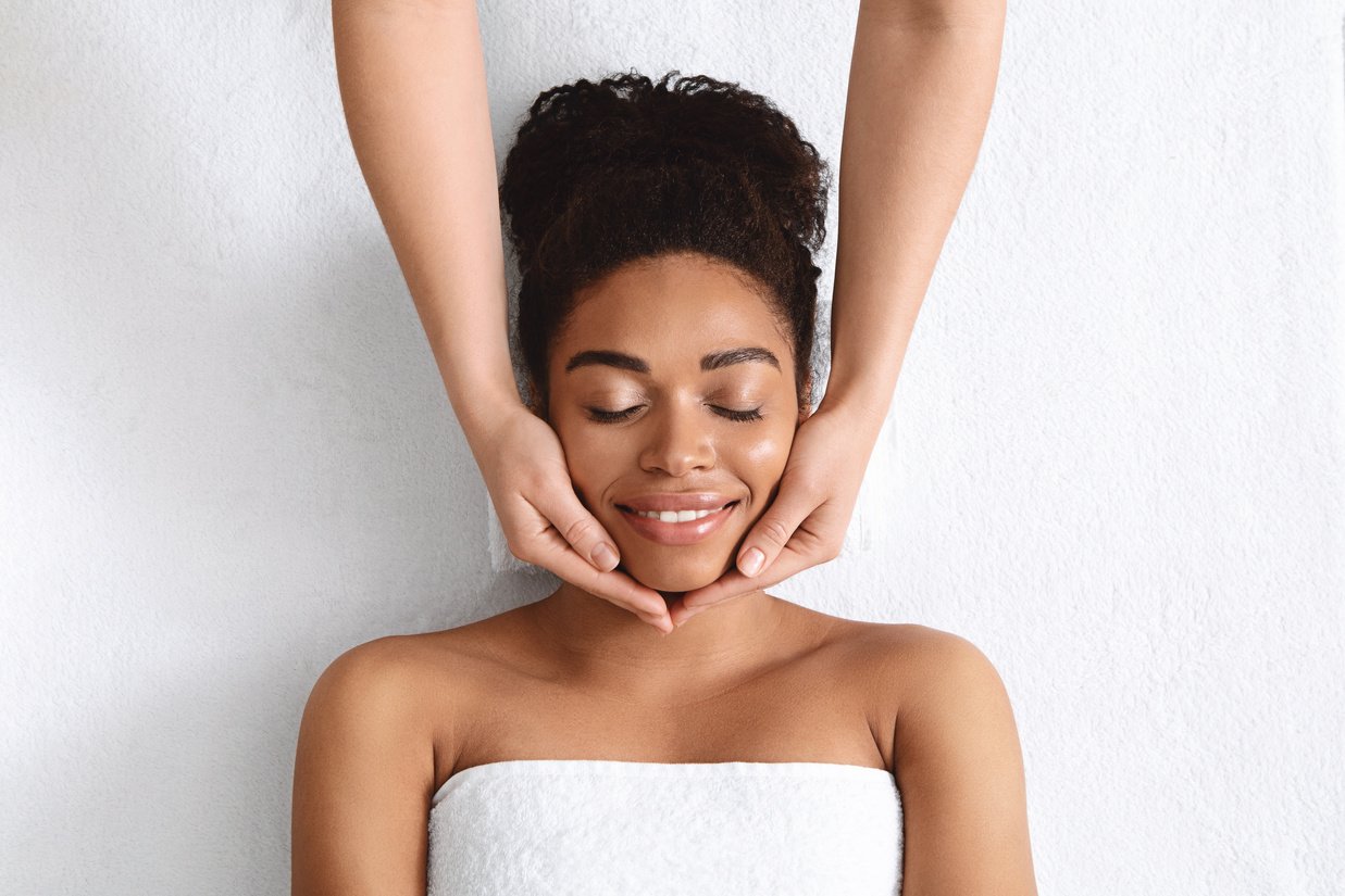 Therapist making lifting facial massage for beautiful black lady